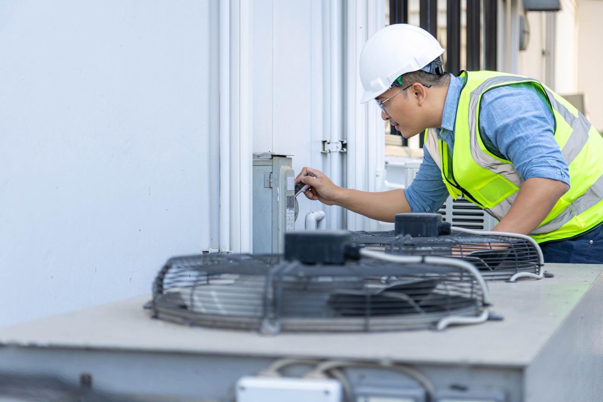A technician in safety gear adjusts a control panel on an outdoor HVAC unit.