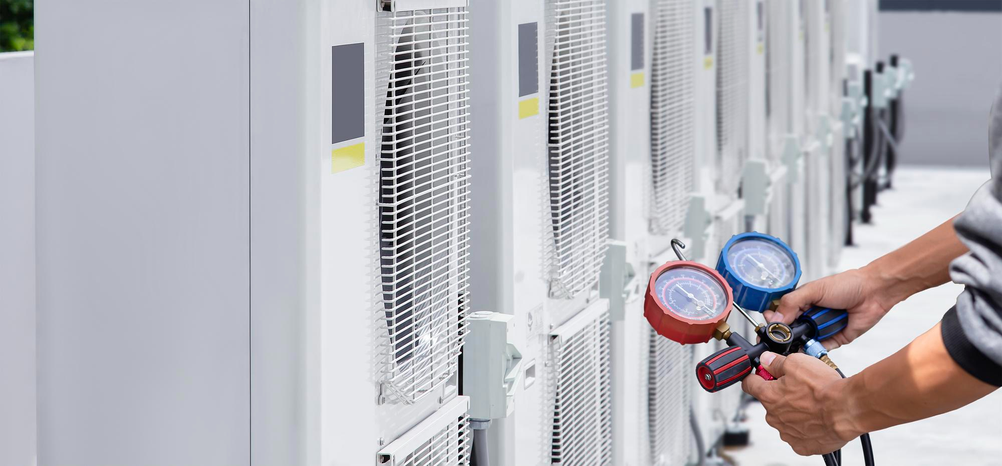 A technician uses a manifold gauge set to service a row of outdoor HVAC units.